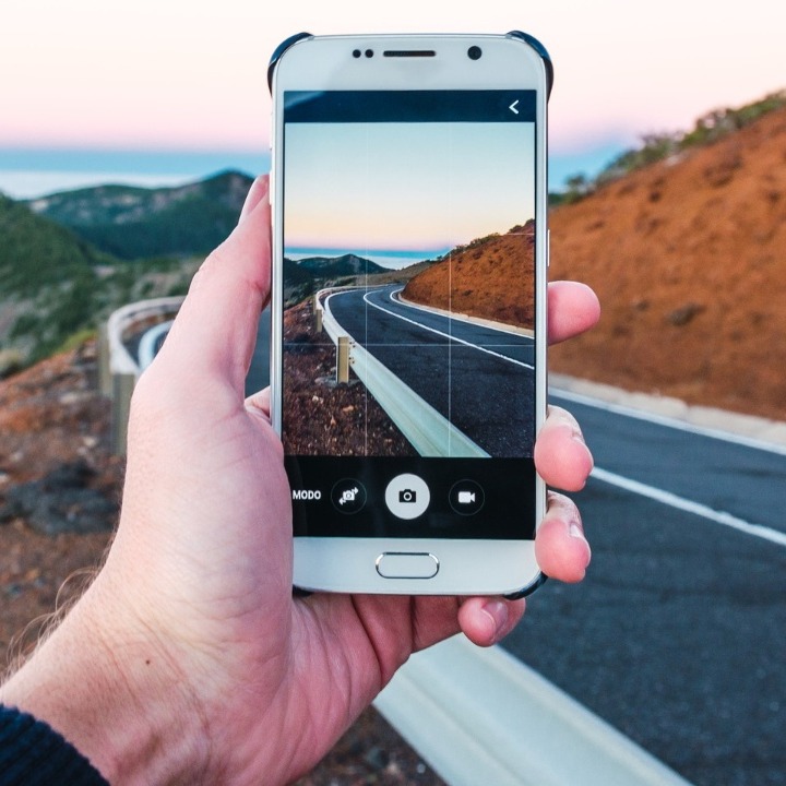 Una mano sosteniendo un móvil para hacer una foto del paisaje de una carretera de montaña
