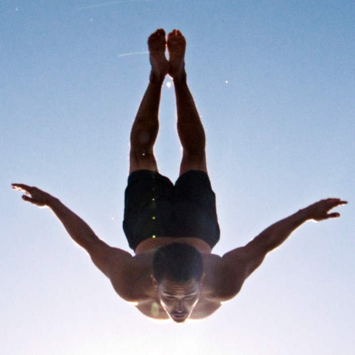 Un hombre haciendo un salto al agua con los brazos en cruz