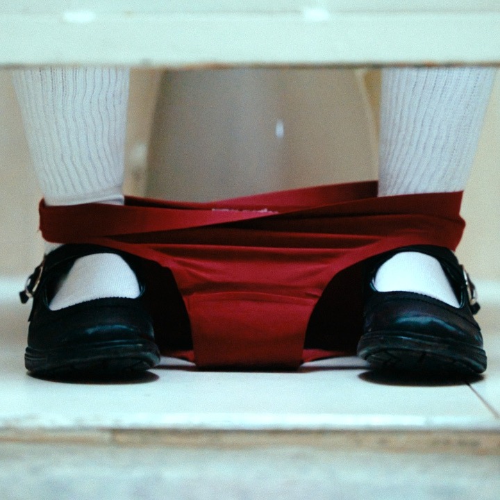 Los pies de una niña en el aseo con las braguitas rojas bajadas