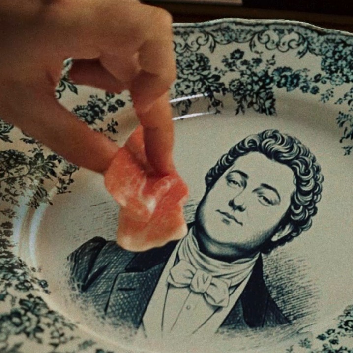 una mano cogiendo un trozo de jamón de un plato de porcelana con ilustraciones en azul