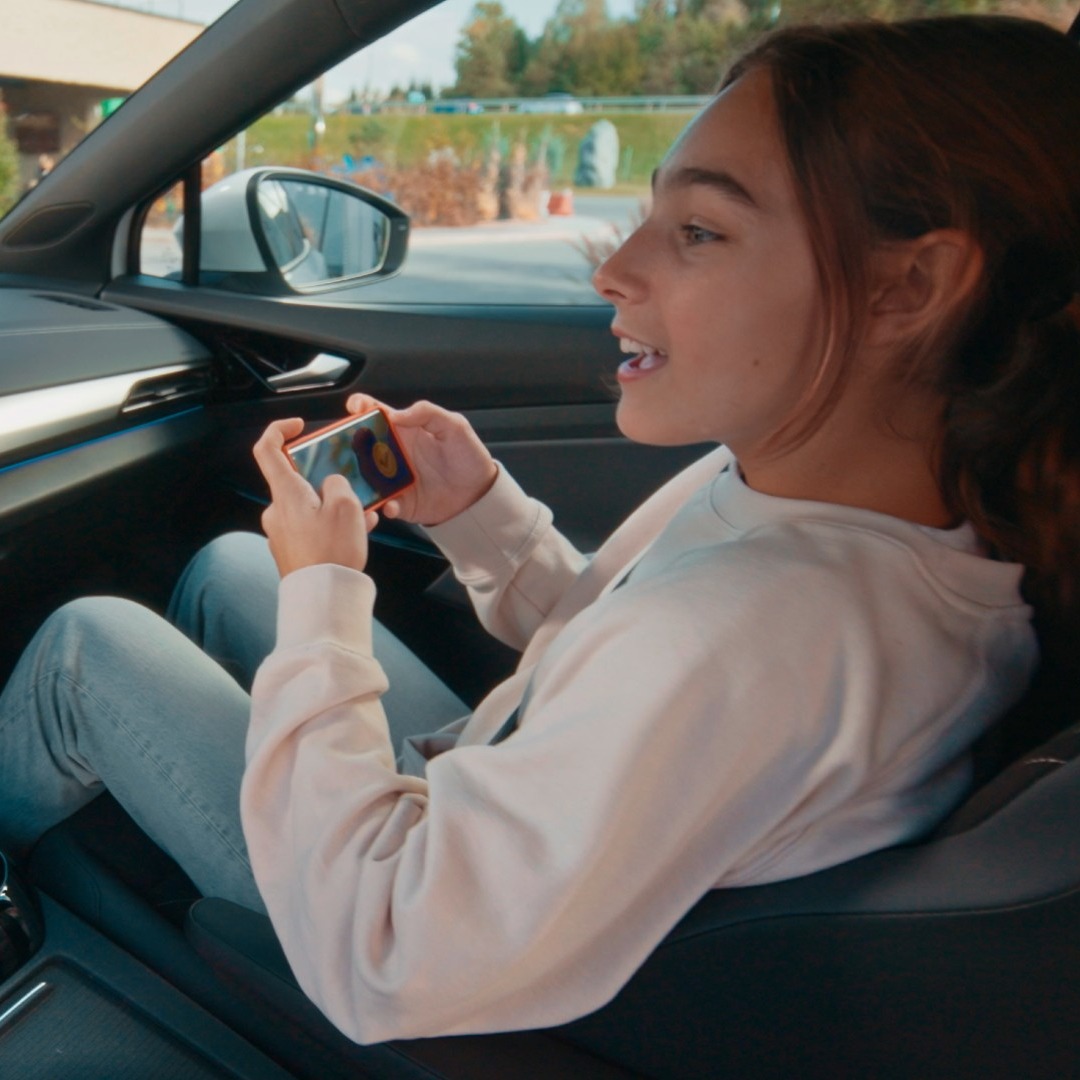 Una joven jugando a Pac-Man con el móvil desde el asiento de copiloto de un coche Volkswagen