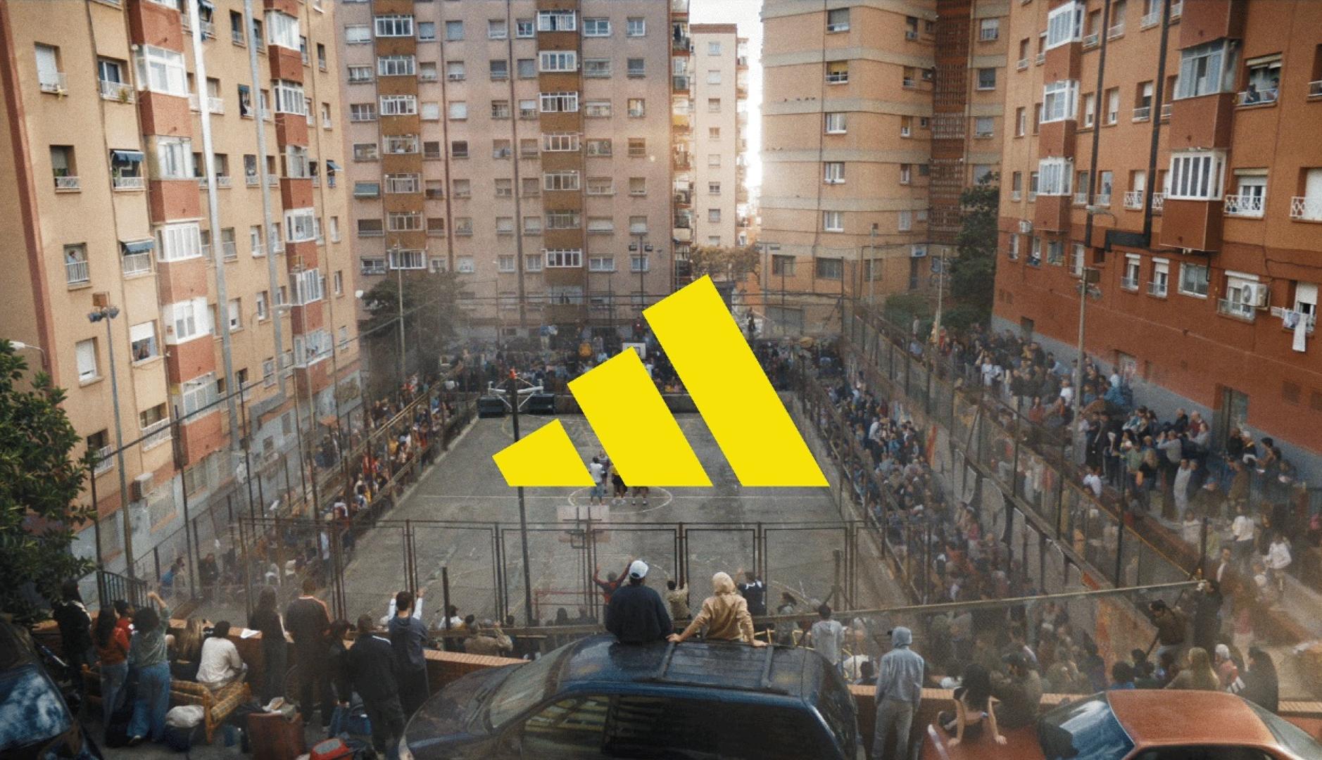 El logo de Adidas en amarillo sobre una cancha callejera rodeada de gente