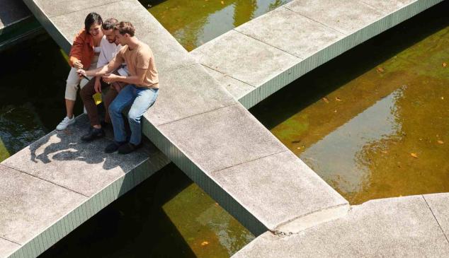 Tres personas miran el móvil sentados en una fuente