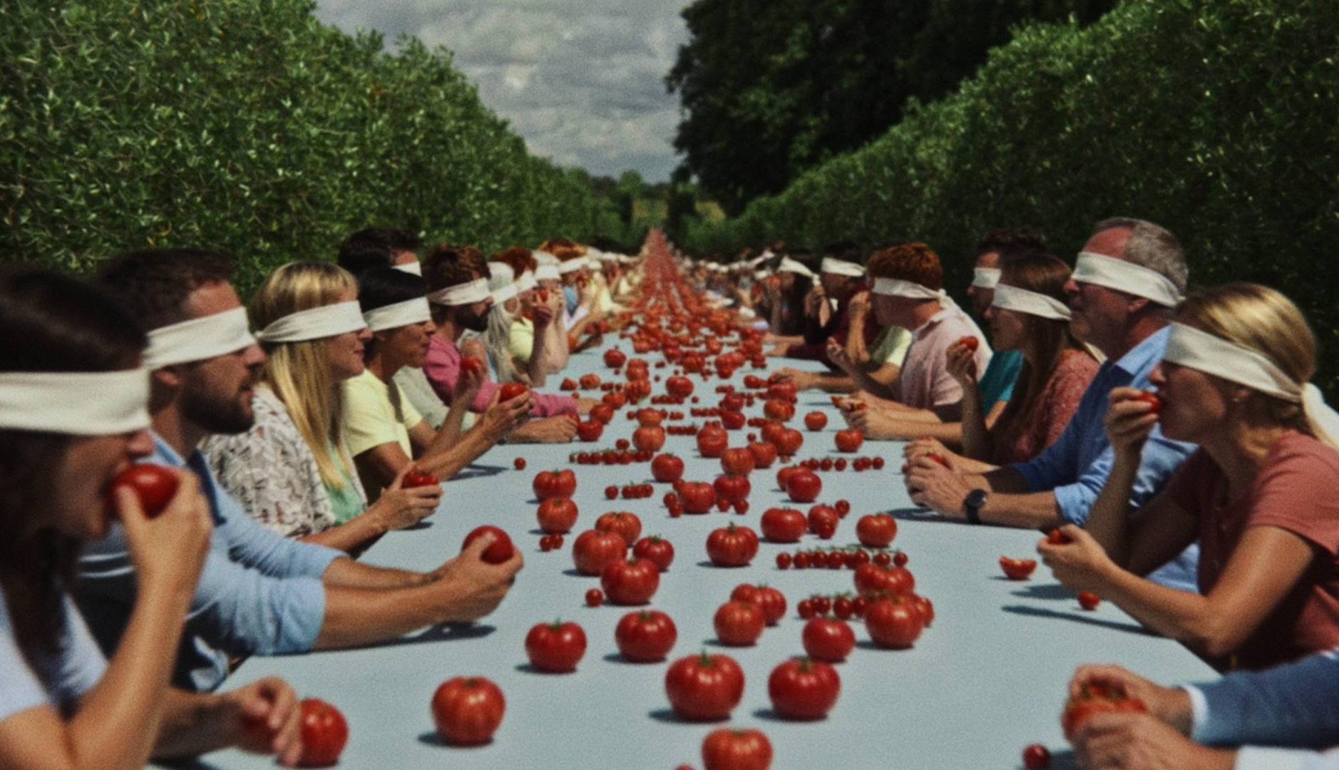 Varias personas sentadas a una mesa con los ojos vendados comiendo tomates