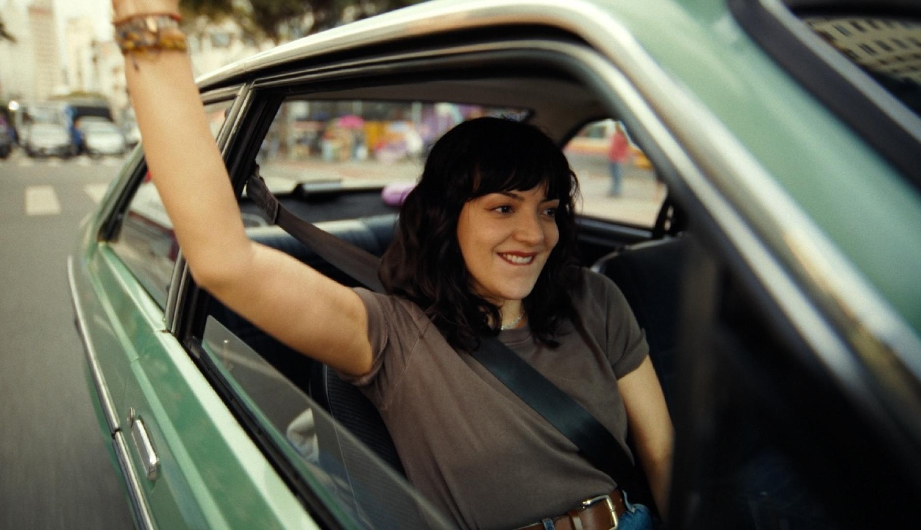 Una mujer levanta el brazo por la ventanilla mientras conduce