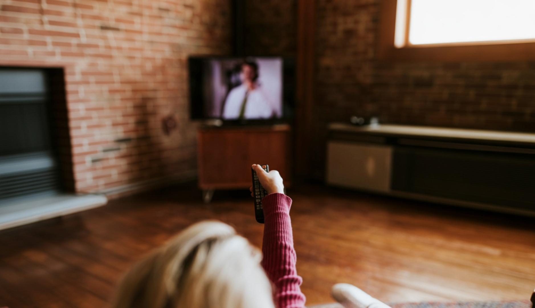 Una mujer sujeta un mando a distancia mientras ve la televisión