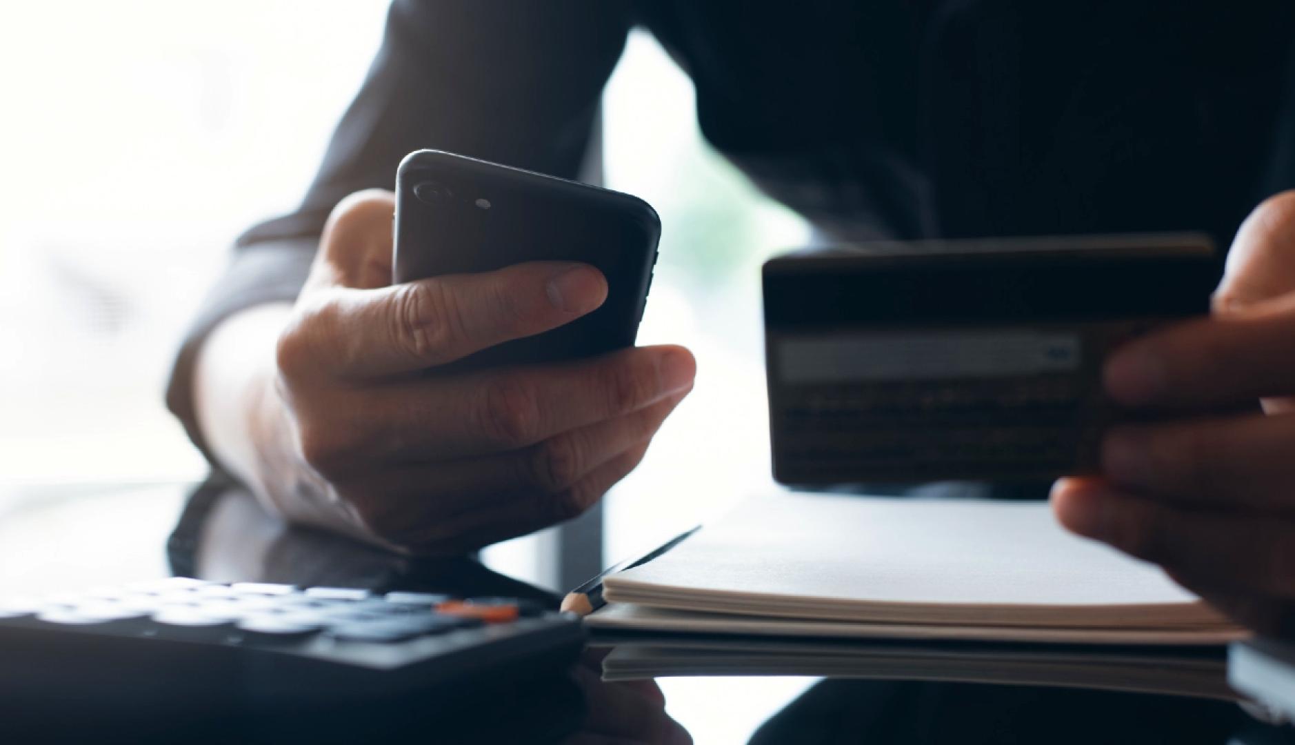 Una mano sostiene un móvil y la otra una tarjeta de crédito