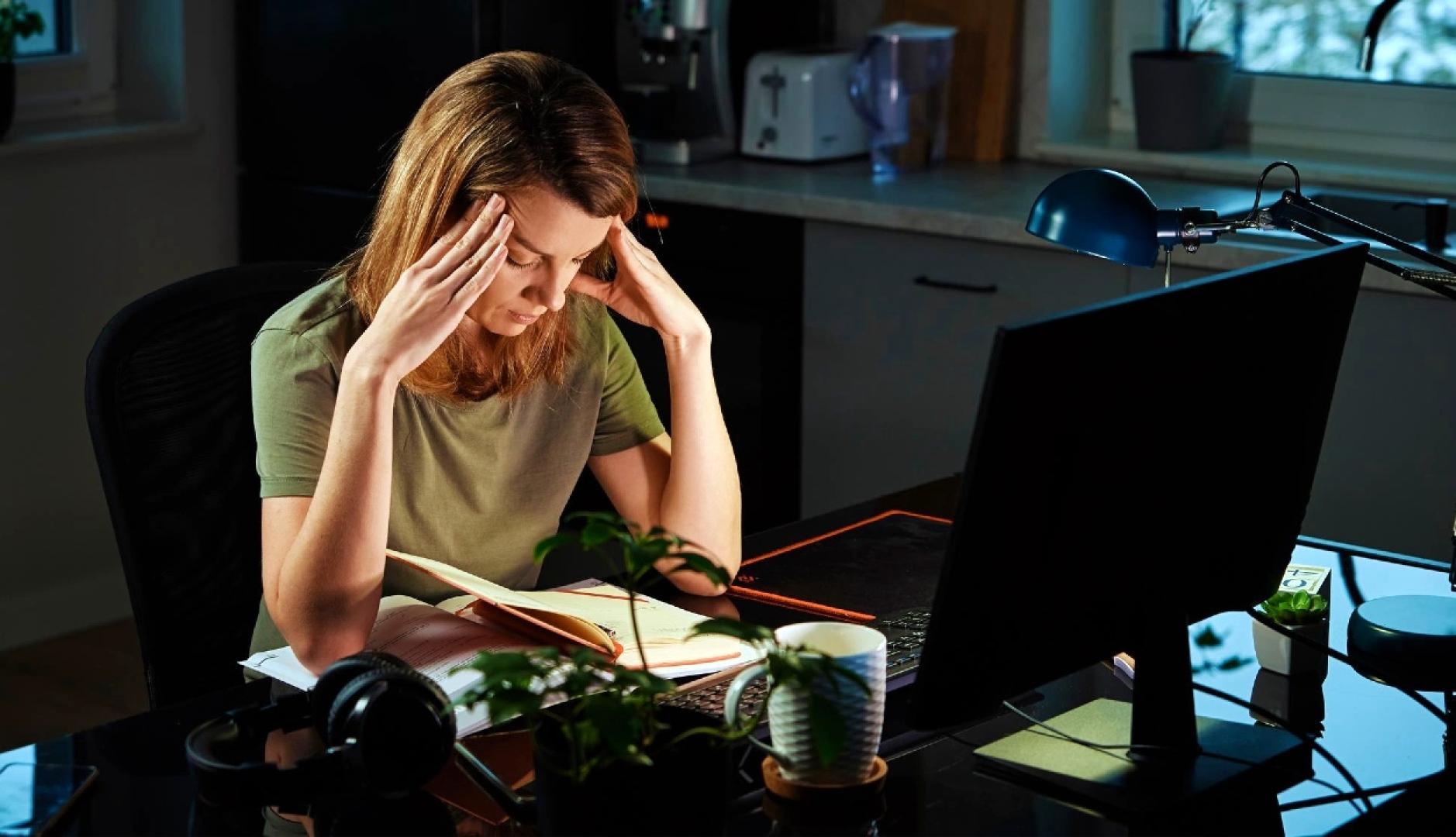 Una mujer que se lleva las manos a la cabeza en un gesto de agotamiento delante del ordenador en la cocina de su casa