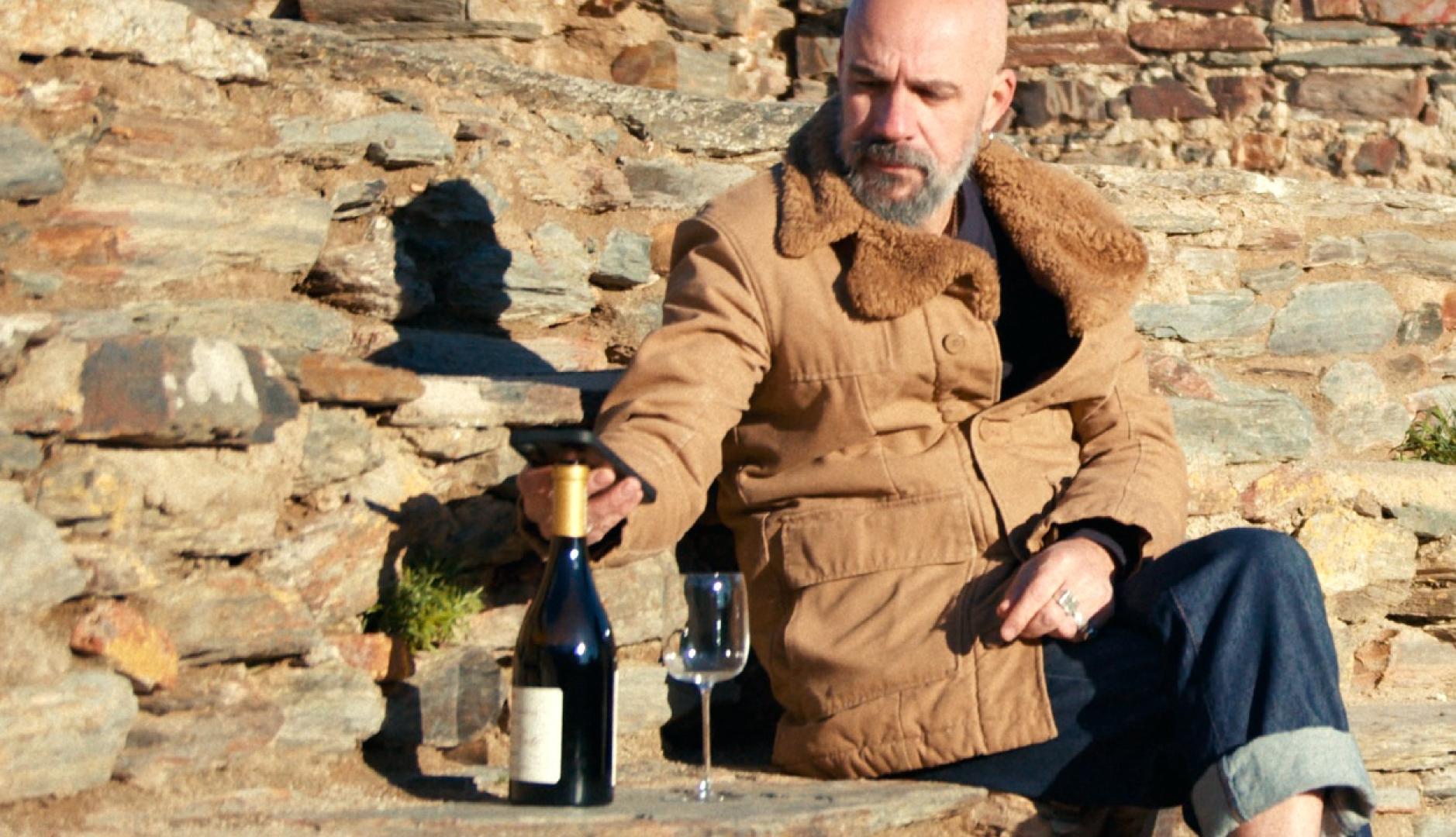 Un hombre sentado al sol acercando el móvil al corcho de una botella de vino