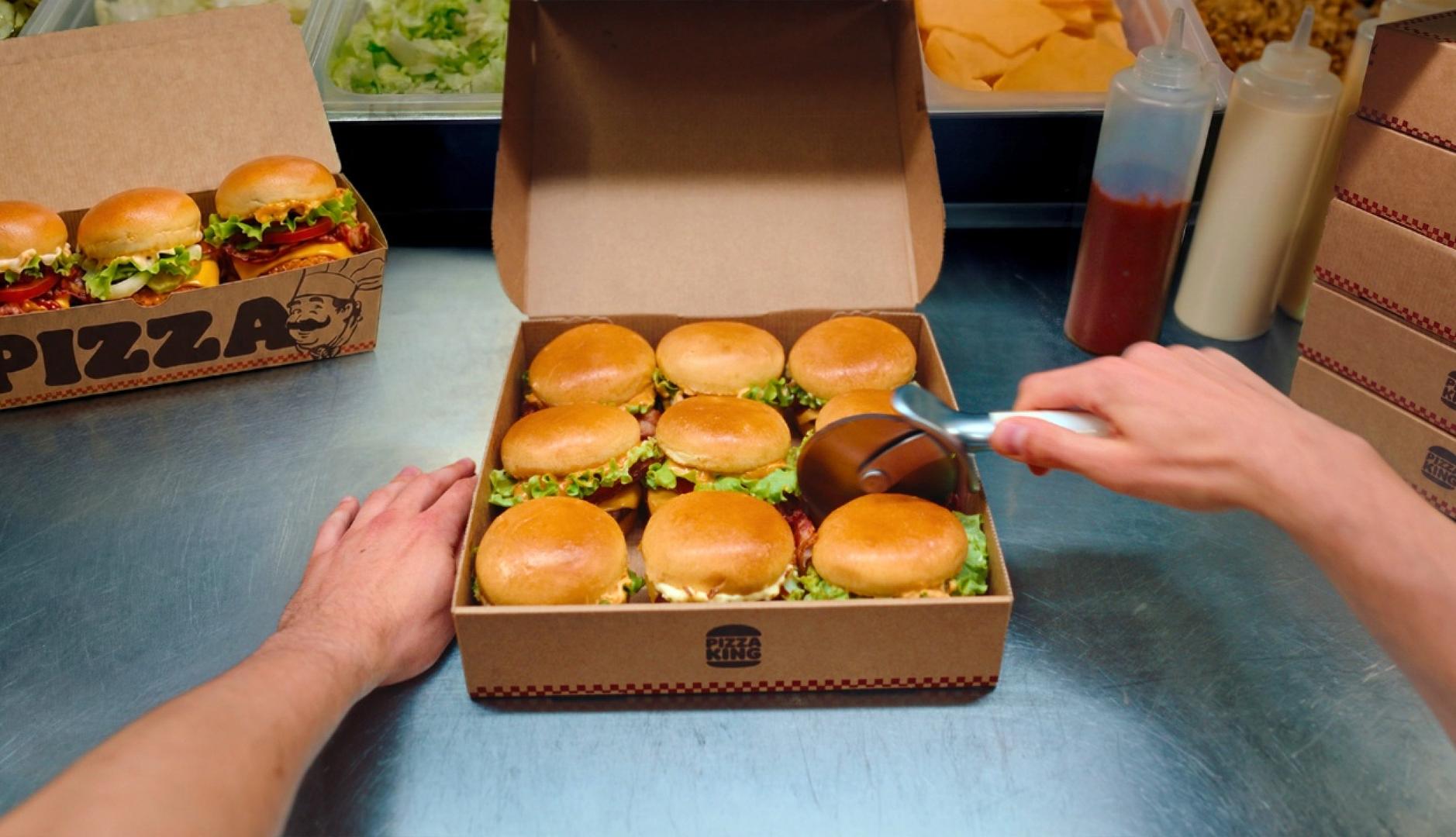 9 mini hamburguesas en una caja cuadrada y una mano con el rodillo de cortar pizza
