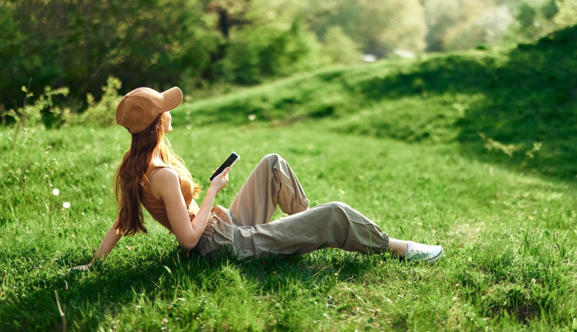 Una chica con gorra sentada en el campo con un teléfono en la mano