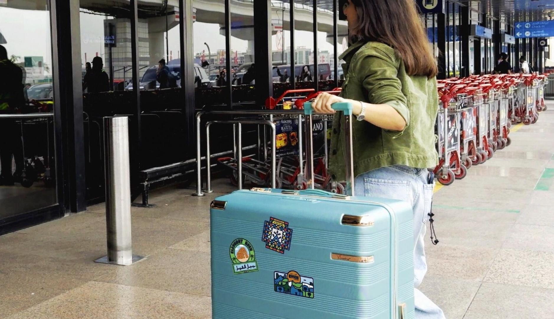 Una chica entrando al aeropuerto con una maleta grande