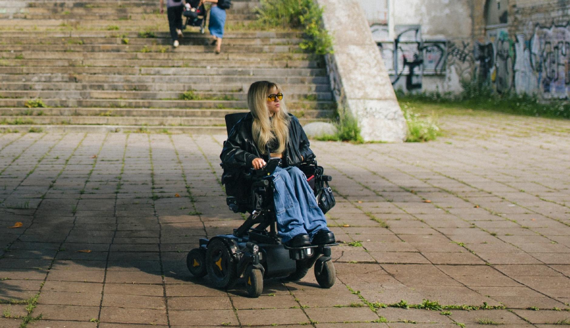 Una chica en silla de ruedas y unas escaleras detrás