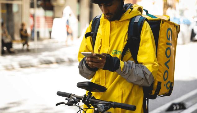 Un repartidor de Glovo en su bici mirando el móvil