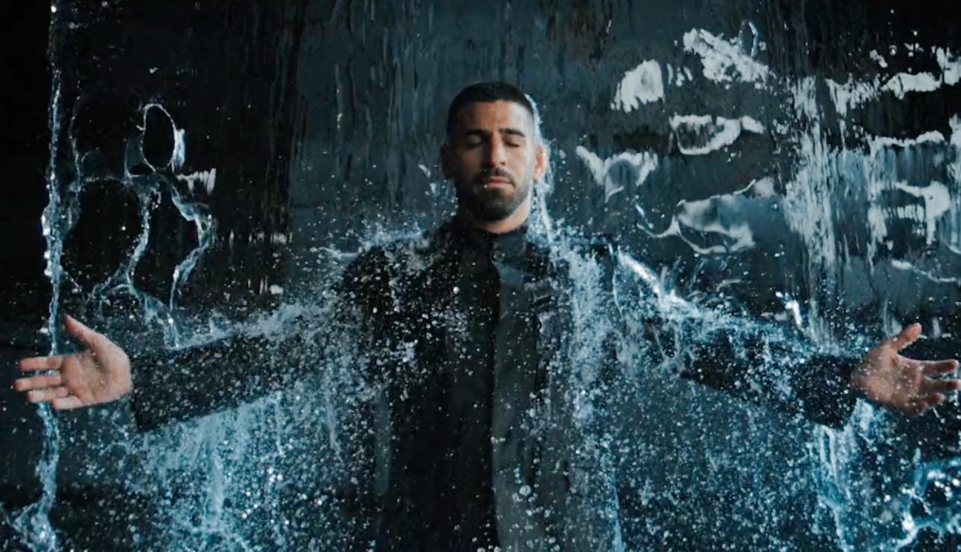 Adolfo Domínguez elige a Ilia Topuria como embajador para comunicar que es “Impermeable” Ilia Topuria con los brazos en cruz bajo una cortina de agua vestido