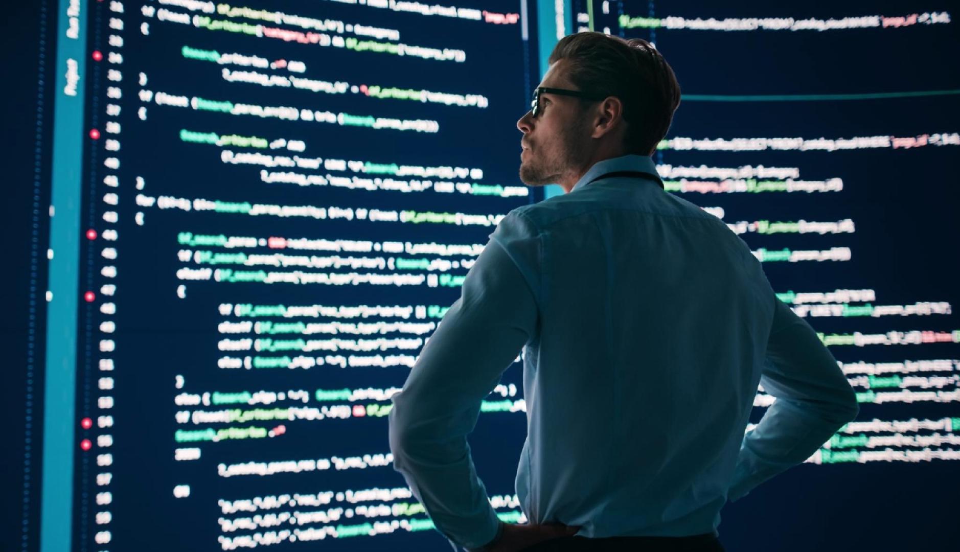Un hombre con los brazos en jarras mira unas pantallas grandes con código HTML