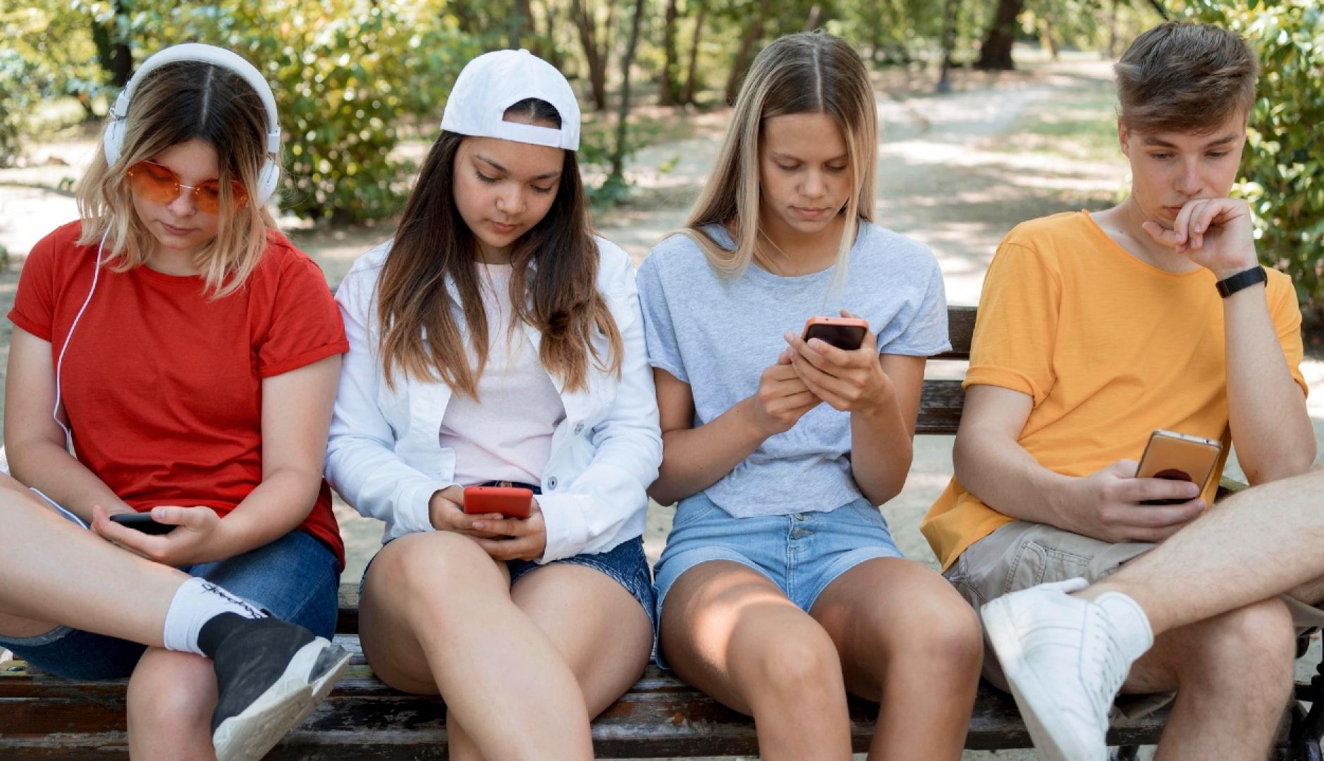 Jóvenes sentados en un banco del parque mirando el teléfono