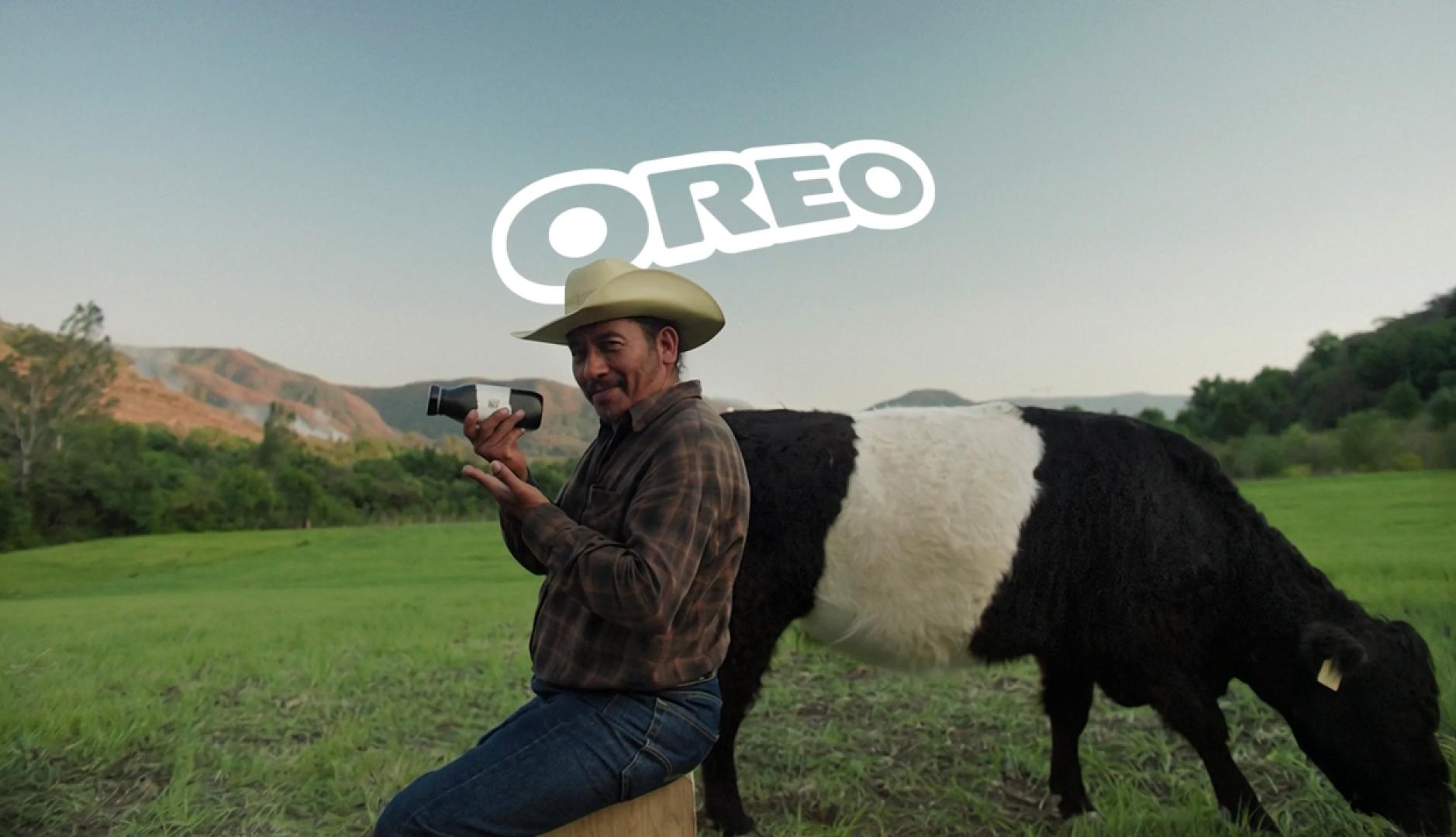 Un granjero posando con la botella de leche de vaca Oreo y detrás una vaca Belted Galloway