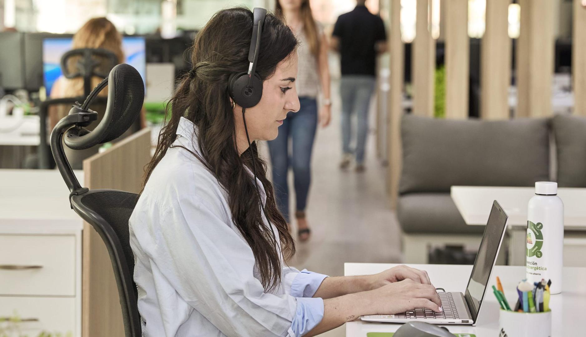 Mujer trabajando delante del ordenador con auriculares