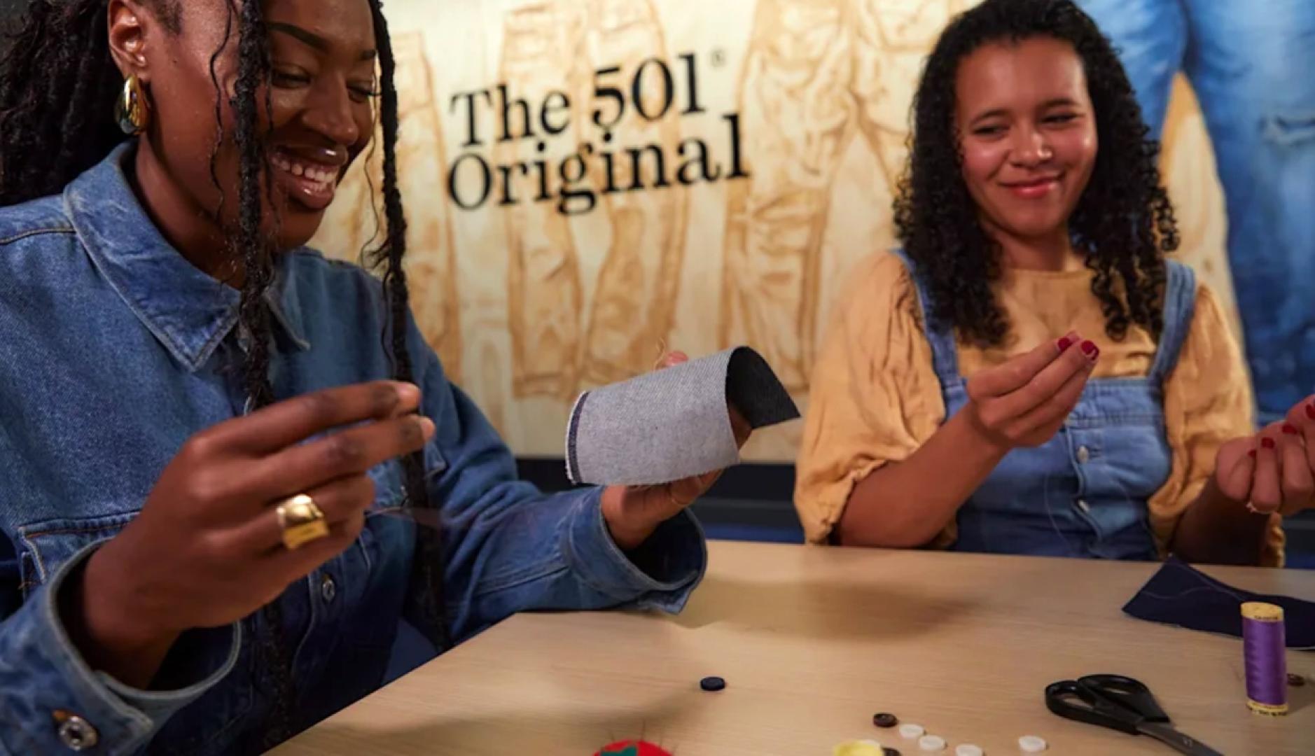 Dos chicas con aguja e hilos riendo mientras intentan coser