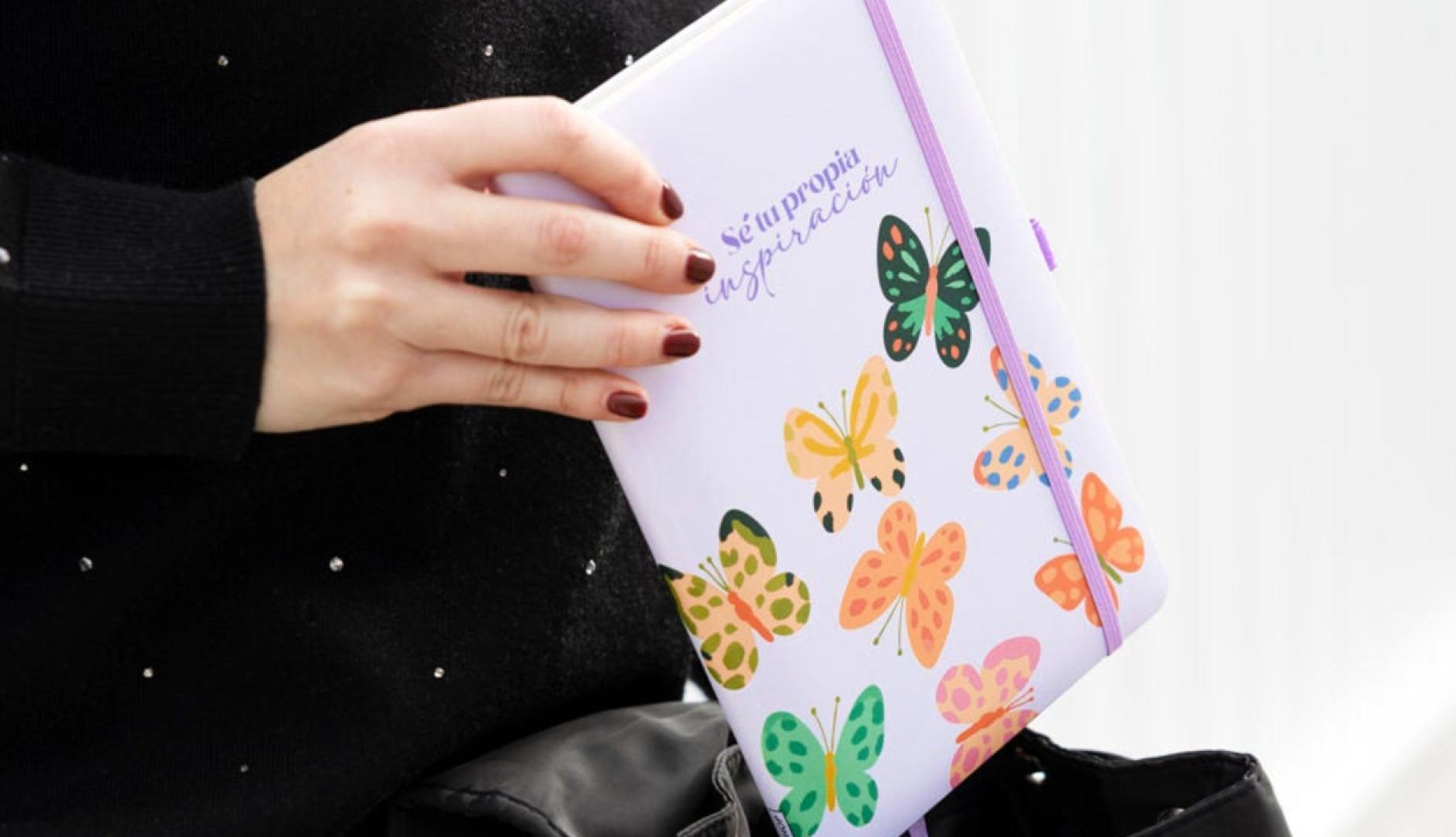 Una mano de mujer sosteniendo una libreta en la que se lee la frase "Sé tu propia inspiración"
