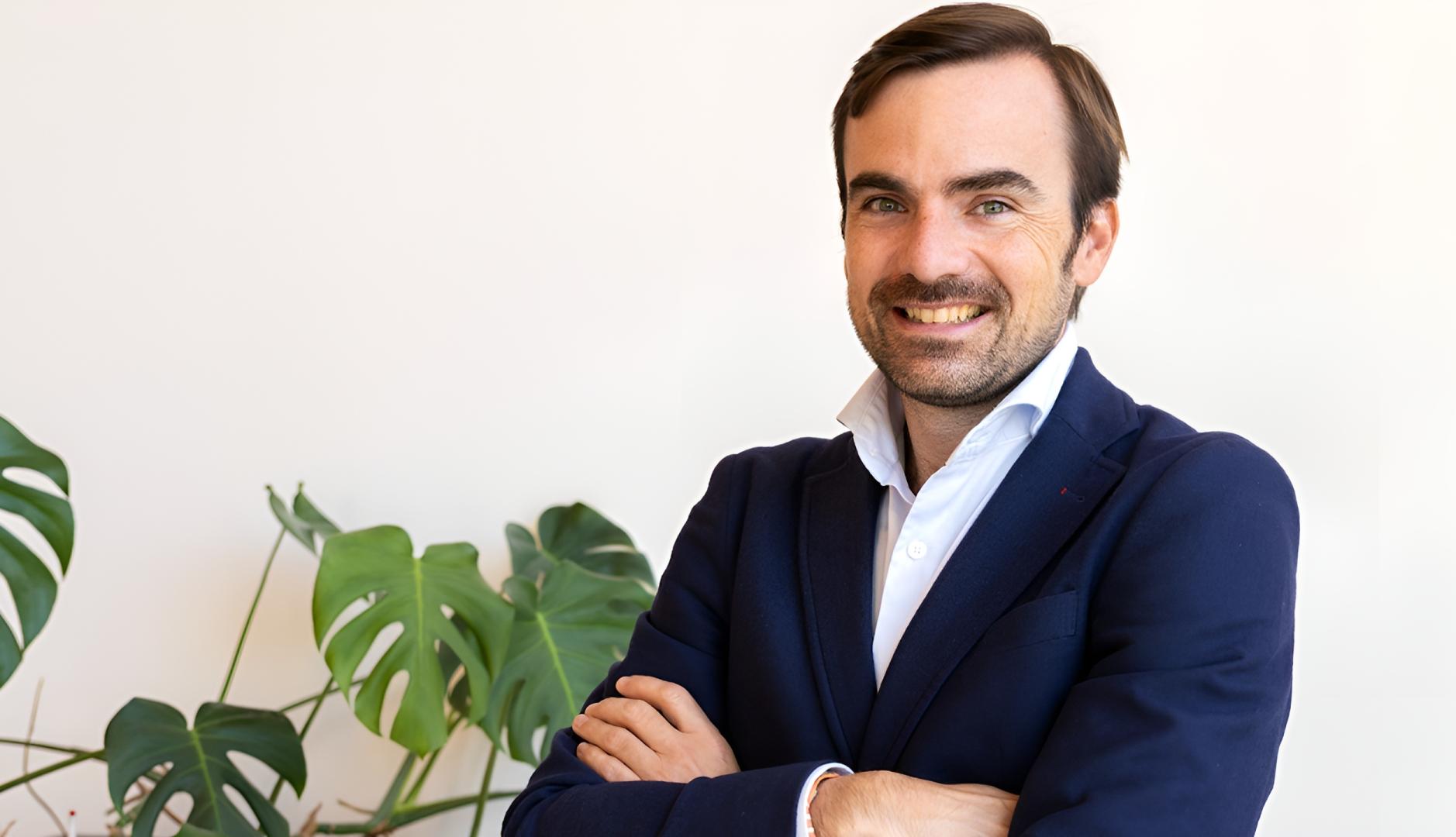 Posado corporativo de Nacho Navarro en traje y con los brazos cruzados al lado de una planta