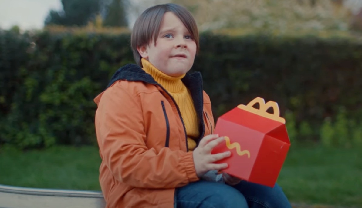 niño sentado con una caja del happy meal y cara de confusión