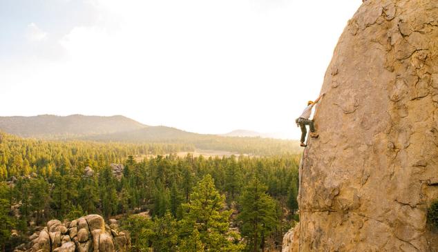 Hombre escala una montaña al atardecer con un bosque al fondo