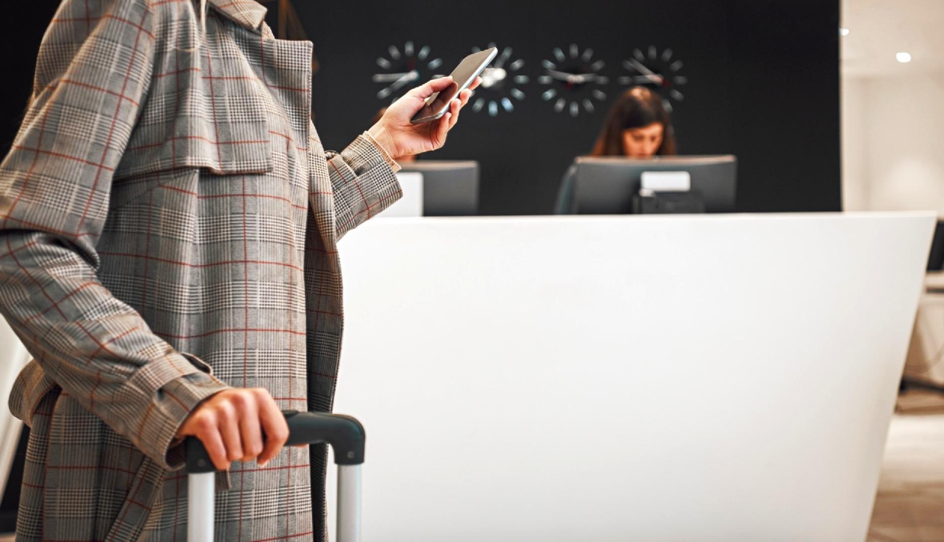 Una mujer con maleta en la recepción del hotel usando el móvil