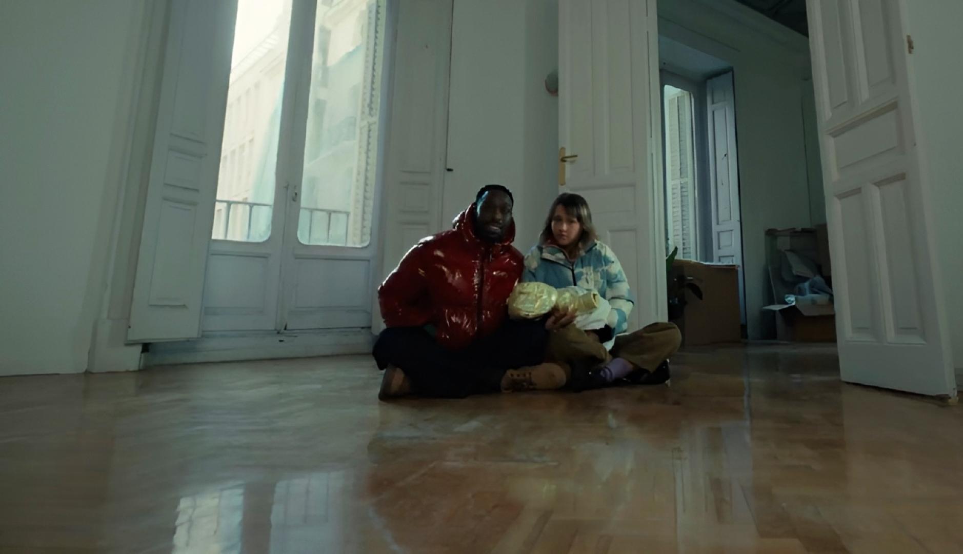 Una pareja sentada en el suelo de un salón vacío con su bebé en brazos