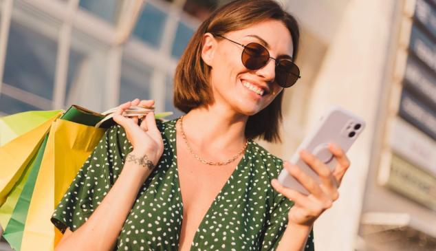 Chica joven con bolsas en la mano mira su teléfono móvil