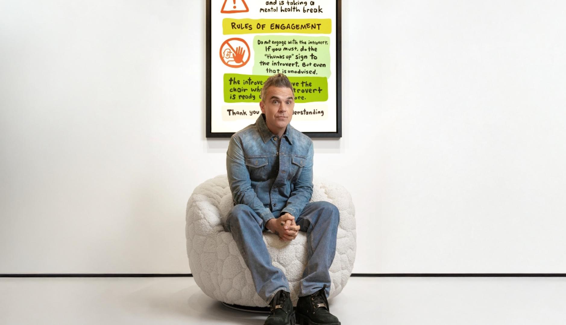 Robbie Williams se refugia en el diseño para hablar de salud mental con “The Introvert Chair” El músico Robbie Williams sentado en la butaca blanca junto al manifiesto para introvertidos
