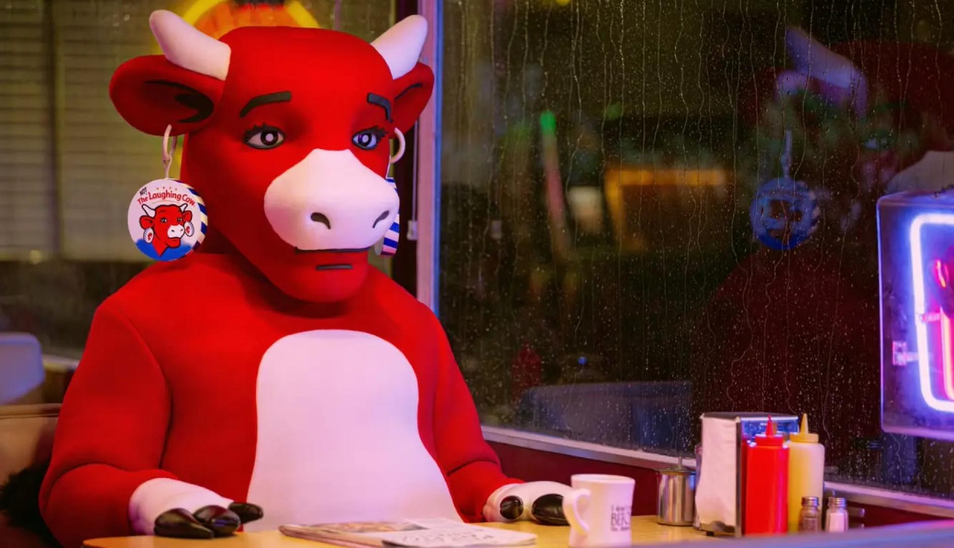 La vaca sentada en un bar con una cristalera lluviosa y el rostro triste