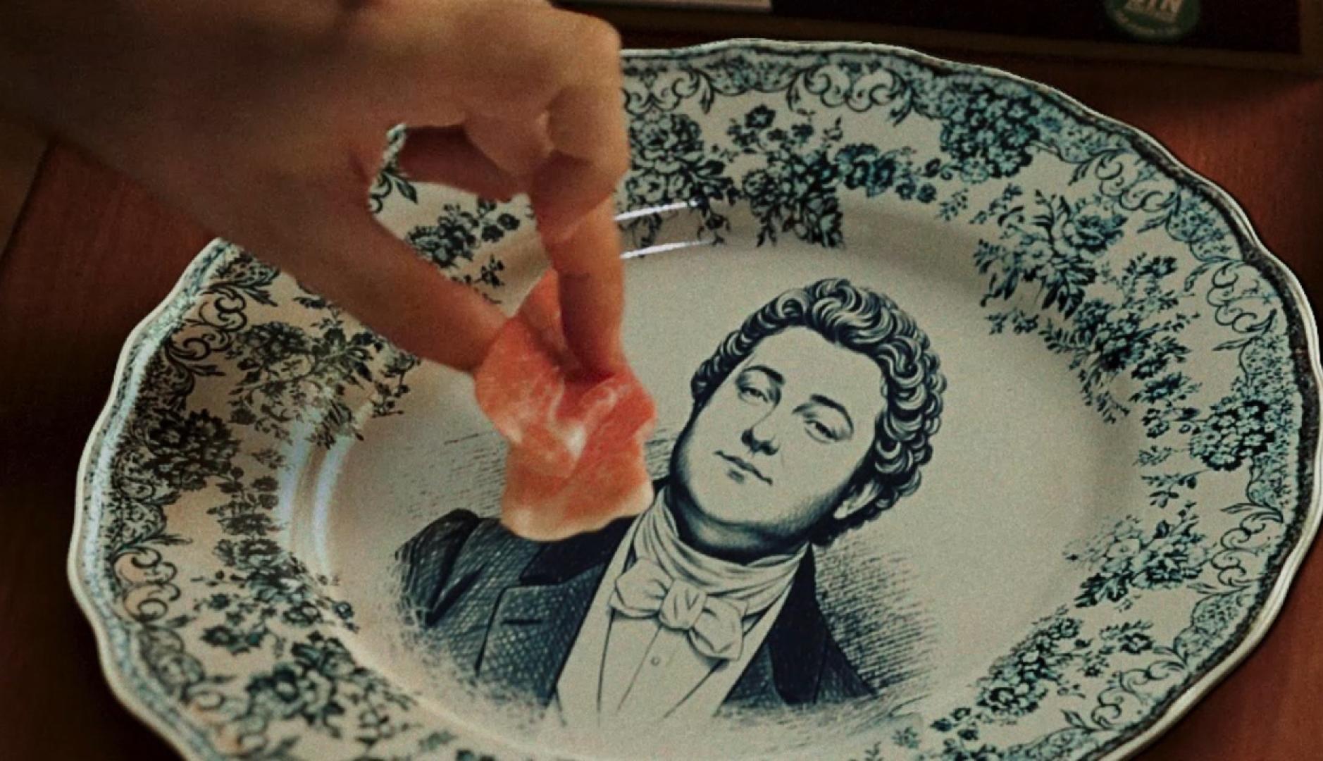 una mano cogiendo un trozo de jamón de un plato de porcelana con ilustraciones en azul