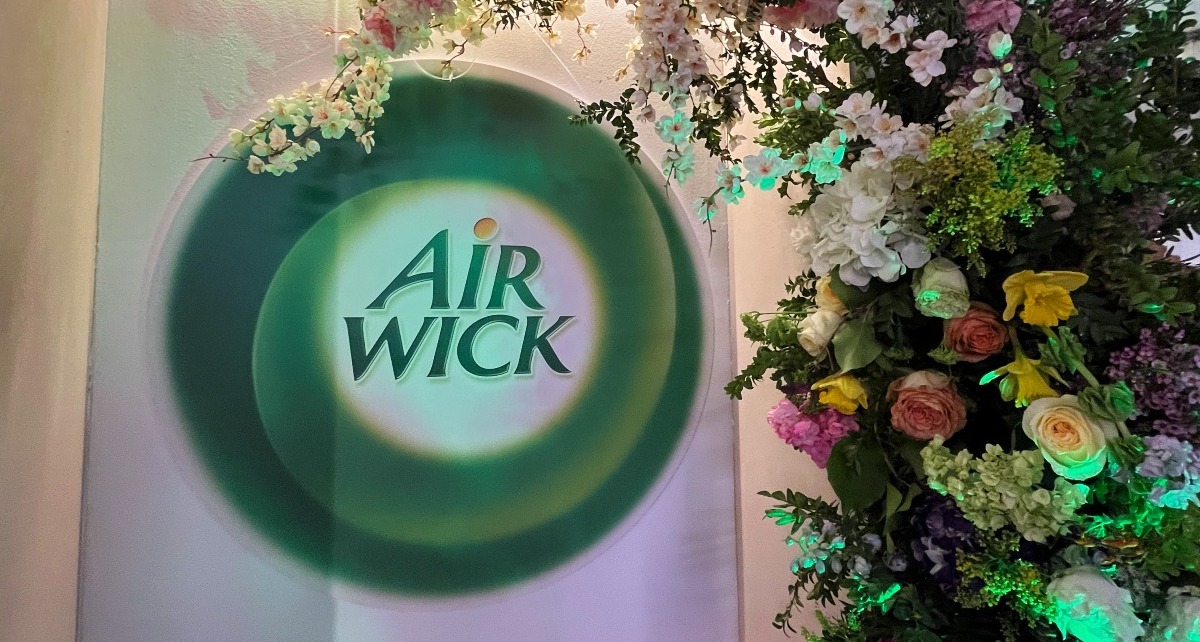 El logotipo de Air Wick junto a una pared de flores de colores