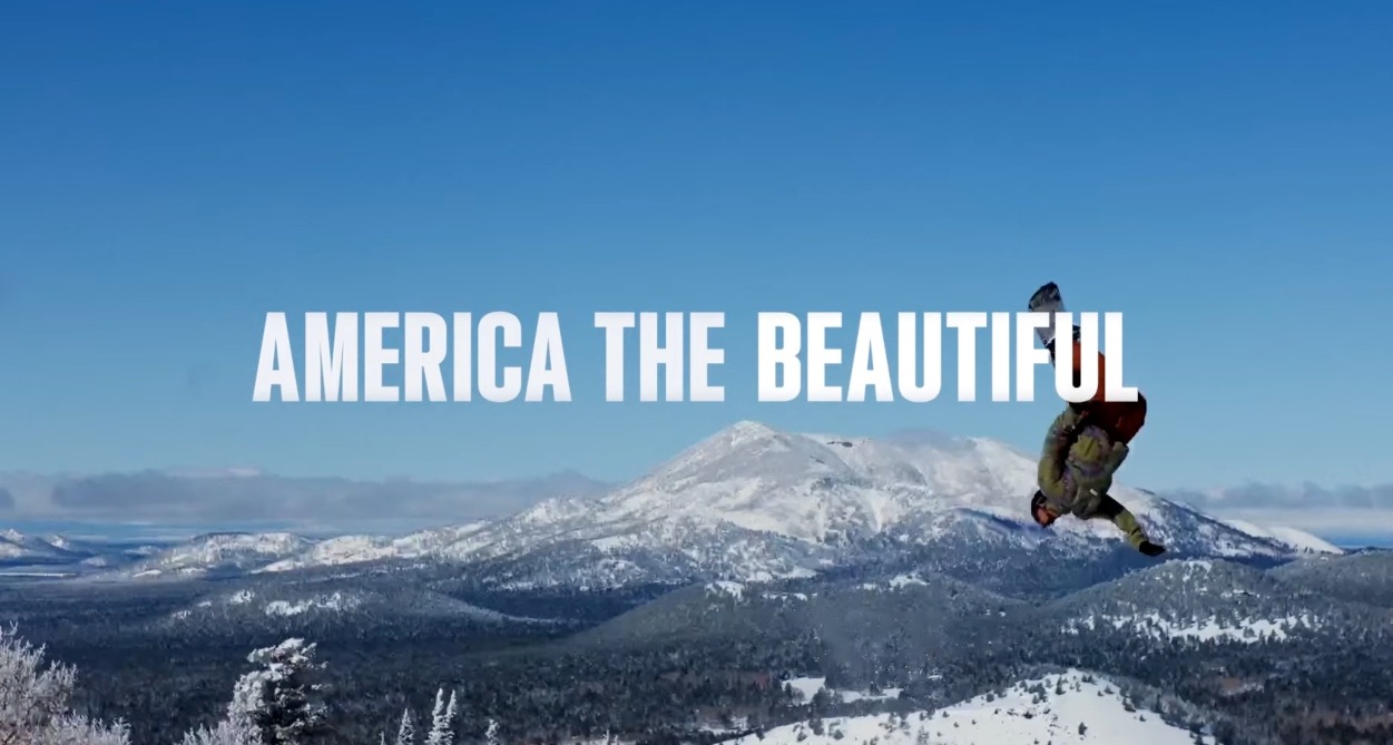 Un hombre haciendo snowboard en la nieve con las letras sobreimpresas de "America the beautiful"