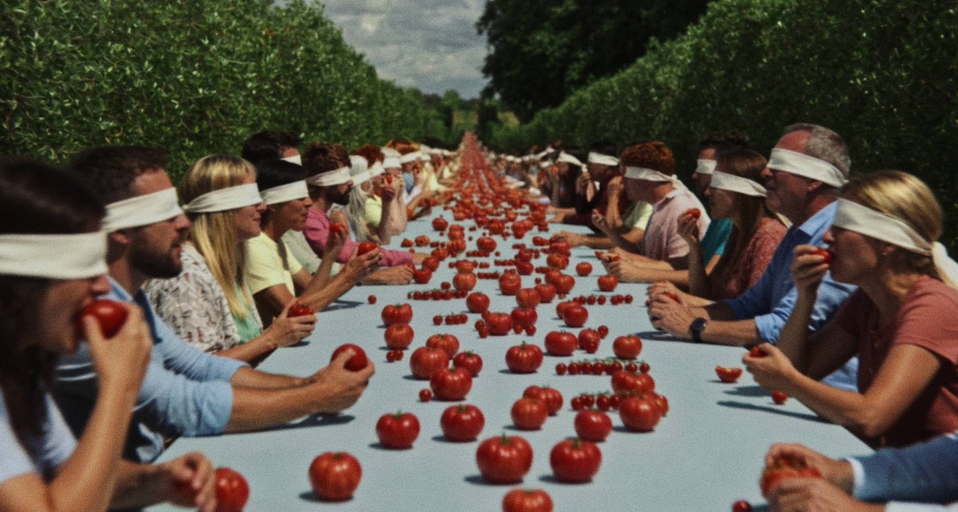 Varias personas sentadas a una mesa con los ojos vendados comiendo tomates