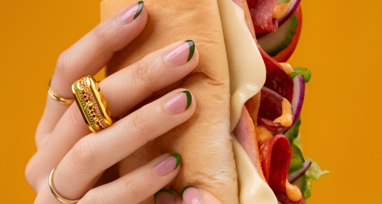Unas manos sosteniendo el sándwich de Subway y en un dedo puede verse el anillo de oro con forma de baguette