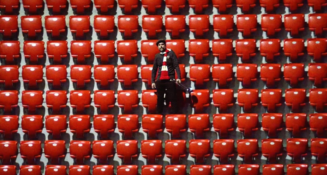 Un hombre en la grada rodeado de sillas rojas vacías