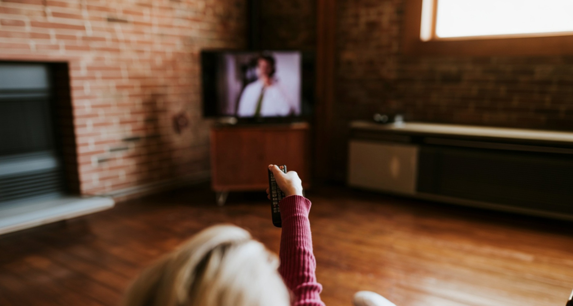 Una mujer sujeta un mando a distancia mientras ve la televisión