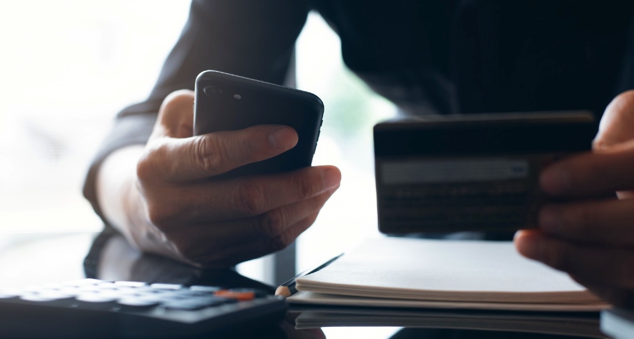 Una mano sostiene un móvil y la otra una tarjeta de crédito