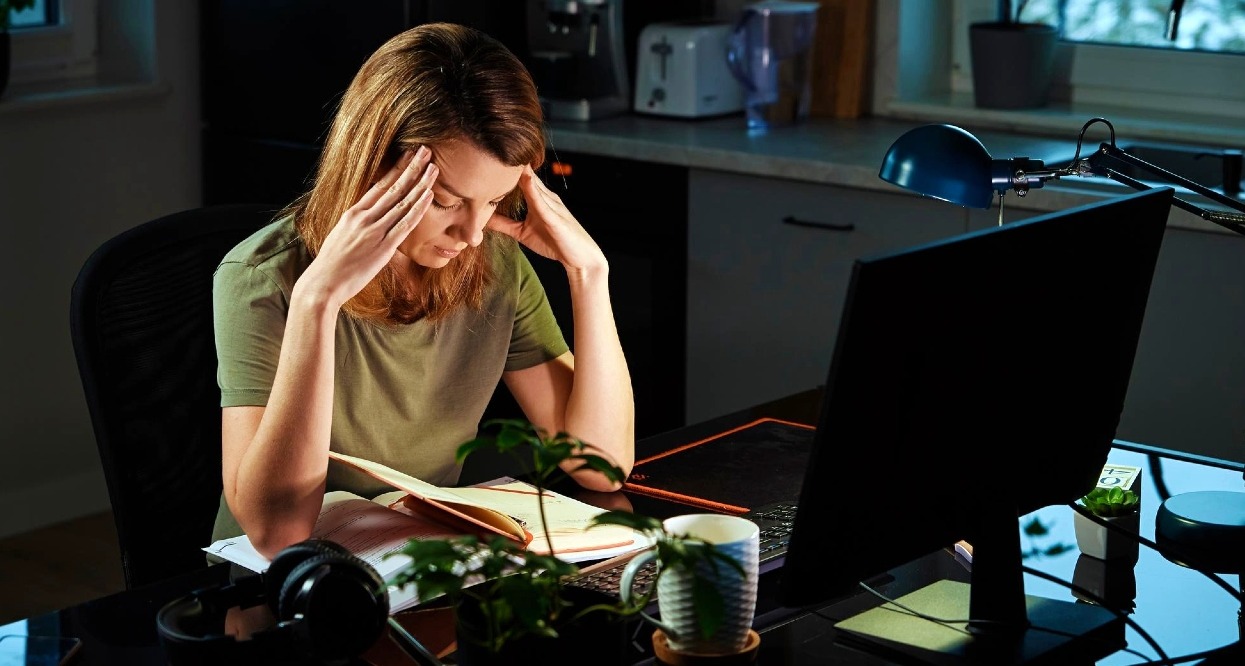 Una mujer que se lleva las manos a la cabeza en un gesto de agotamiento delante del ordenador en la cocina de su casa