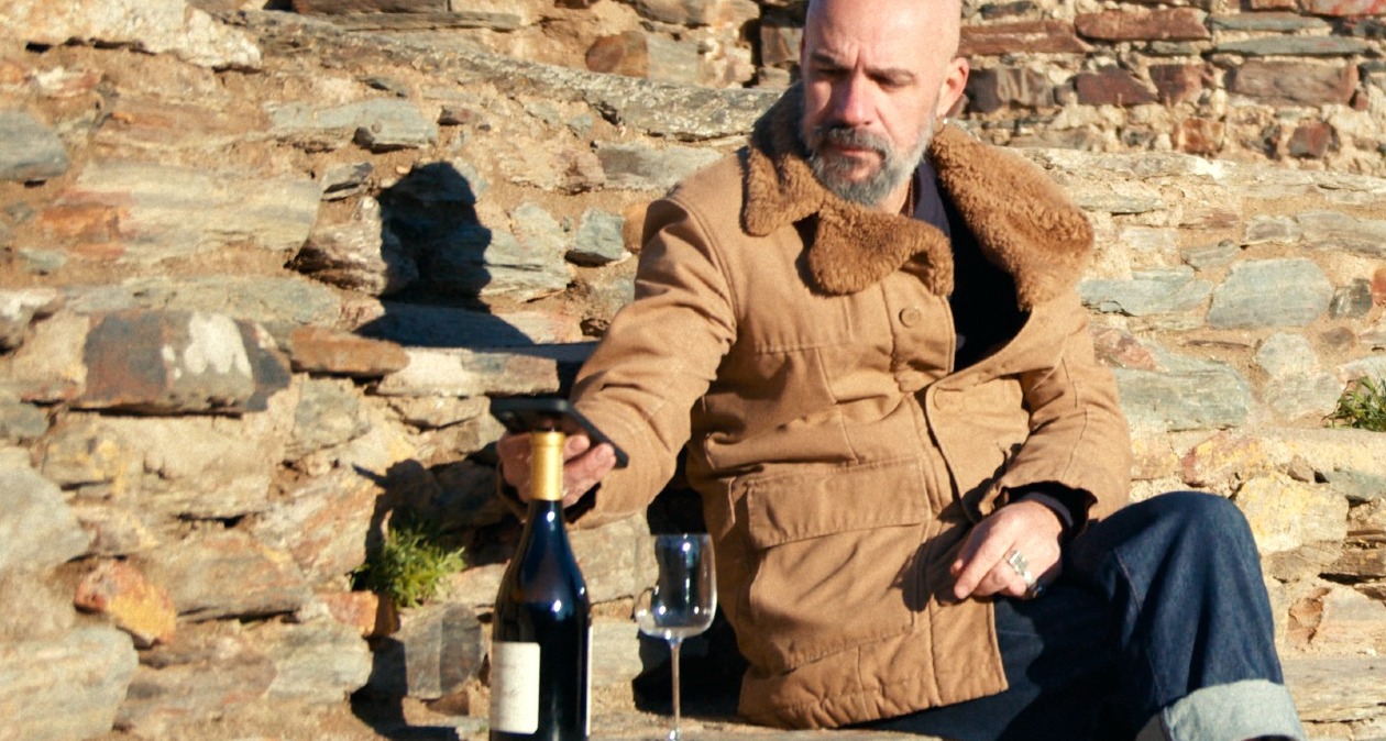 Un hombre sentado al sol acercando el móvil al corcho de una botella de vino