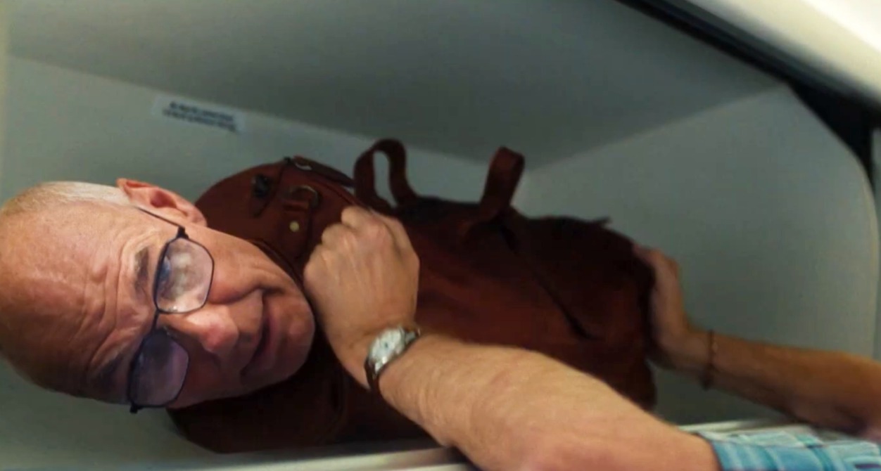 Una maleta con cabeza de señor que se está colocando en el maletero del avión