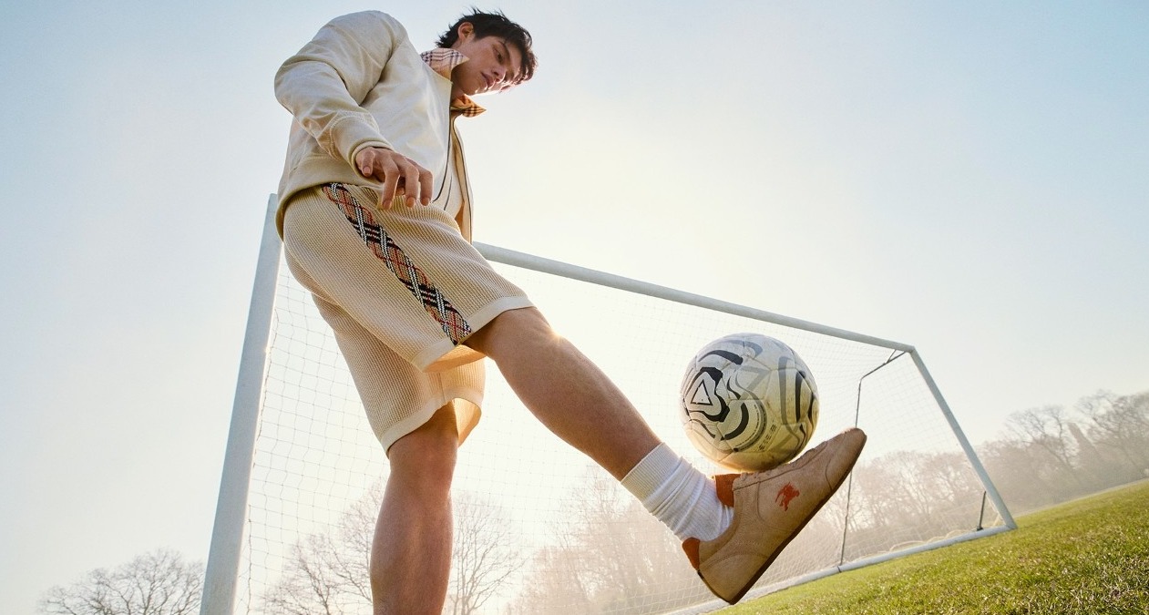 Un chico vestido de Burberry junto a una portería de fútbol dando un toque al balón