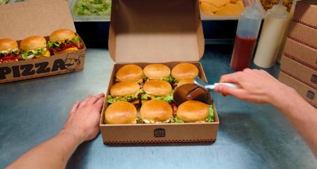 9 mini hamburguesas en una caja cuadrada y una mano con el rodillo de cortar pizza