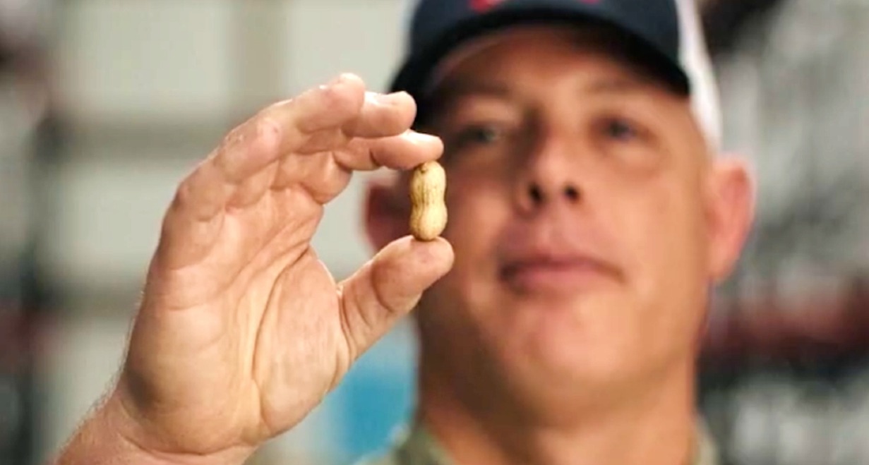 Un hombre con gorra sostiene un cacahuete con cáscara en la mano