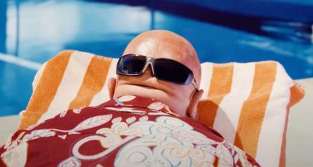 Persona calva tomando el sol en una piscina boca abajo, con unas gafas de sol sobre la nuca