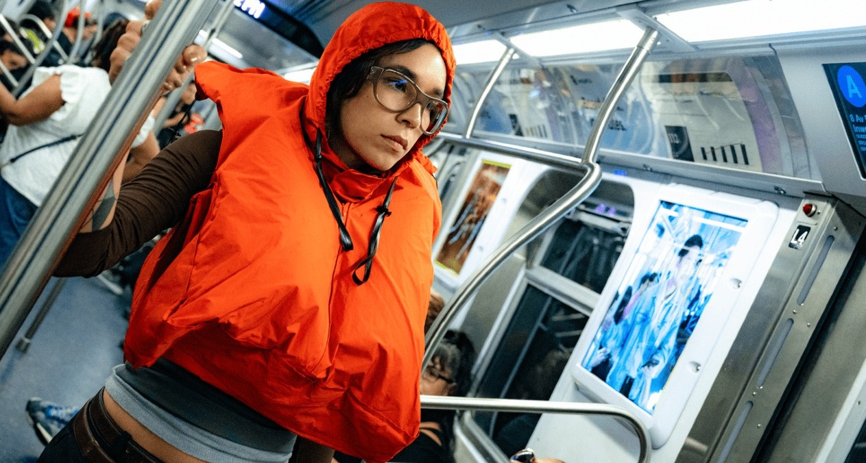 Una chica en un vagón de metro con el chaleco naranja puesto