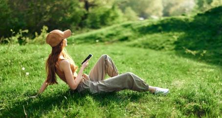 Una chica con gorra sentada en el campo con un teléfono en la mano
